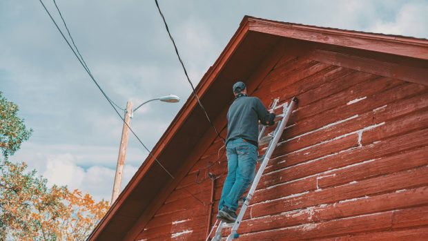 A person standing on a ladder clearing leaves from the gutter of a house